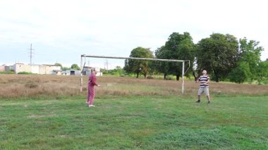 Eski futbol kalelerinin yakınındaki bir sahada badminton oynayan iki kişi, açık havada eğlencenin tadını çıkarıyorlar..