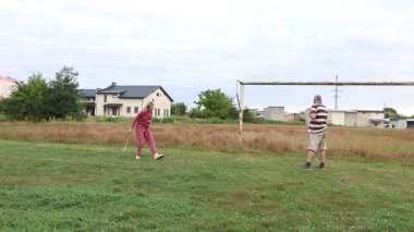 Eski futbol kalelerinin yakınındaki bir sahada badminton oynayan iki kişi, açık havada eğlencenin tadını çıkarıyorlar..