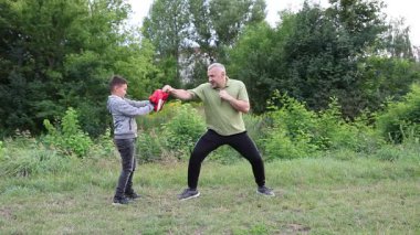 Çocuk, Green Park 'ta yetişkin koçuyla boks antrenmanı yapıyor..