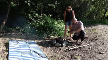 Erkek ve kadın dışarıda barbekü hazırlamak için ateş yakıyor. Açık havada piknik..