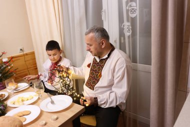 İşlemeli gömlekler içindeki baba ve oğul yemek ve süslemeler arasında şenlik masasında otururlar..