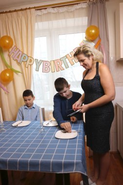 Oğlu ve yeğeniyle birlikte bir kadın doğum günü kutlaması için festival masası hazırlıyor. Yumuşak ışıklandırma.
