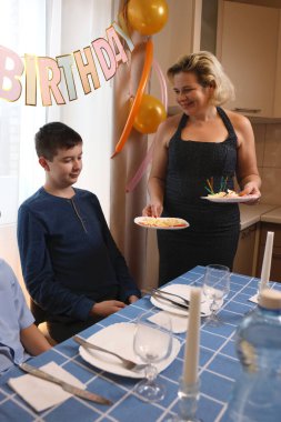 Oğlu ve yeğeniyle birlikte bir kadın doğum günü kutlaması için festival masası hazırlıyor. Yumuşak ışıklandırma.