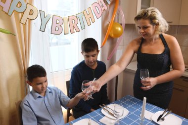 Oğlu ve yeğeniyle birlikte bir kadın doğum günü kutlaması için festival masası hazırlıyor. Yumuşak ışıklandırma.