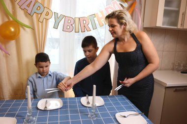 Oğlu ve yeğeniyle birlikte bir kadın doğum günü kutlaması için festival masası hazırlıyor. Yumuşak ışıklandırma.