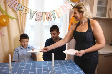 Oğlu ve yeğeniyle birlikte bir kadın doğum günü kutlaması için festival masası hazırlıyor. Yumuşak ışıklandırma.