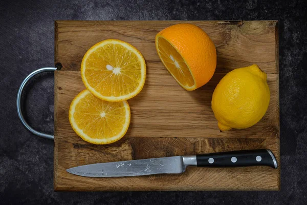 Koyu bir arka planda, tahta bir tabakta, bıçakla taze limon kes..