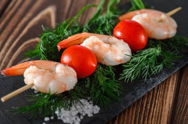 Soyulmuş karides ve kırmızı domates tahta bir çubukta taş kesme tahtası, yiyecek arka planı.