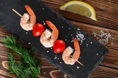 Tahta çubukta domatesli karideslerin üst görüntüsü tuz, limon ve dereotlu, yiyecek arka planı.
