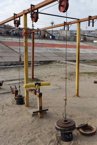 Kablo makaraları ve yeniden tasarlanmış araba parçalarından yapılmış ağırlıklar içeren açık hava spor aletleri, kumla kaplı bir zemine kurulmuş..
