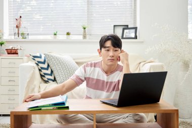 Genç Asyalı Adam Parlak Modern Oturma Odasında Dizüstü bilgisayar ve Klasörlerle Çalışıyor