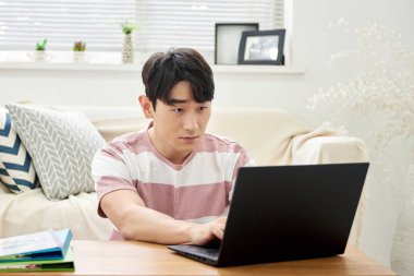 Genç Asyalı Adam Parlak Modern Oturma Odasında Dizüstü bilgisayar ve Klasörlerle Çalışıyor