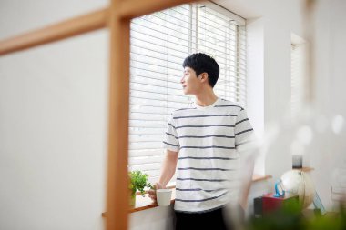 Genç Asyalı Adam Parlak Modern Oturma Odasında Pencere kenarında Kahve İçiyor