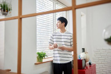 Genç Asyalı Adam Parlak Modern Oturma Odasında Pencere kenarında Kahve İçiyor