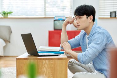 Genç Asyalı Adam Parlak Modern Oturma Odasında Laptop ve Kitapla Çalışıyor