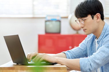 Genç Asyalı Adam Parlak Modern Oturma Odasında Laptop ve Kitapla Çalışıyor