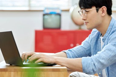 Genç Asyalı Adam Parlak Modern Oturma Odasında Laptop ve Kitapla Çalışıyor