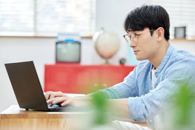 Genç Asyalı Adam Parlak Modern Oturma Odasında Laptop ve Kitapla Çalışıyor