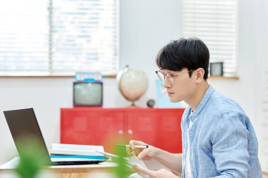 Genç Asyalı Adam Parlak Modern Oturma Odasında Laptop ve Kitapla Çalışıyor