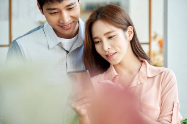 Young Asian Man and Woman Using Smartphone Together in Bright Modern Home