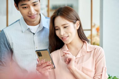 Young Asian Man and Woman Using Smartphone Together in Bright Modern Home
