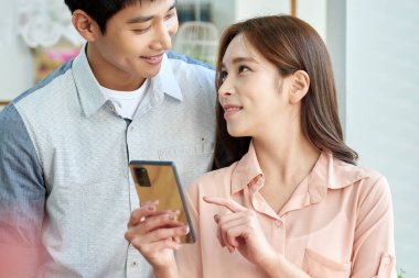 Young Asian Man and Woman Using Smartphone Together in Bright Modern Home