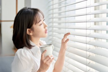 Genç Asyalı Kadın Sabahları Pencere kenarında Bir fincan kahvenin tadını çıkarıyor