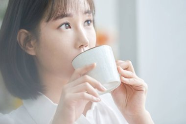 Genç Asyalı Kadın Sabahları Pencere kenarında Bir fincan kahvenin tadını çıkarıyor