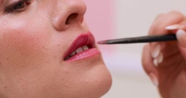 Güzellik salonundaki makyaj seansı sırasında bir müşterinin dudaklarını dikkatlice boyayan bir güzellik uzmanının elleri.