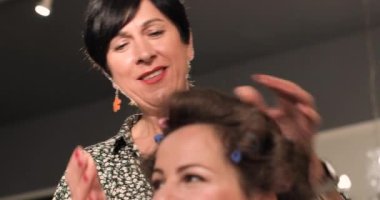 Bir kuaför kuafördeki müşterinin saçına saç spreyi sürüyor, tarıyor ve kullanıyor.