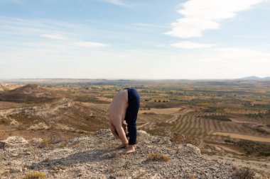 Bir adam Uttanasana, ya da Ayakta İleriye Bükülme, bir yoga seansı sırasında gerilme için, sahada ve doğa