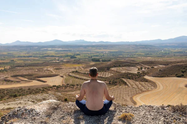 在一个瑜伽课上 一个男人在一个巨大的乡村景观前 从山顶上 以帕面萨纳的姿势沉思着 — 图库照片