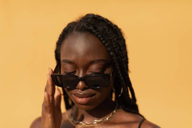 Güneş batımında güneş gözlüğünden aşağıya bakan genç siyahi bir kadının yakın plan portresi.