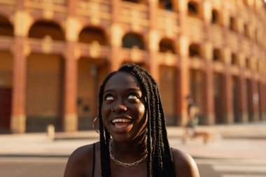 Gün batımında sokaklarda modellik yaparken şapşal suratlar yapan genç siyahi bir kadının yakın plan portresi.