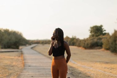 Young black female talking on the phone in the park during a beautiful summer sunset