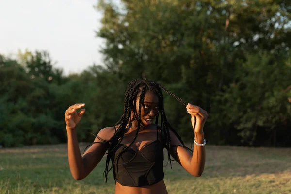 Portrait of a young black female playfuly moving her hair at the park during a beautiful sunset