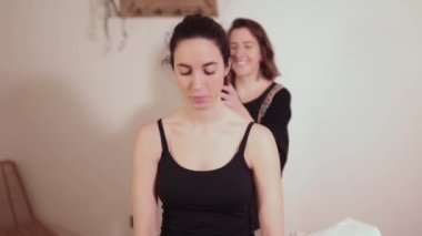 A woman therapist examines her patients shoulders and neck, on the massage table, before beginning the chiromassage that will dissipate her back pain