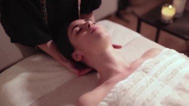 A masseuse massages the neck of her patient who is lying face up on the chiro table to relieve her health issues and muscle pain