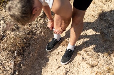 Bir adam çoraplarını çekip güneşli bir günde kırlarda koşmaya hazırlanıyor.