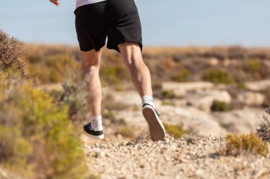 Orta yaşlı bir adamın bacaklarına yakın çekim. Formda kalmak ve sağlıklı bir yaşam sürmek için kırsalda koşuyor ve egzersiz yapıyor.