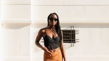 Genç, siyah bir kadın, saçları örgülü, güneş gözlüğü takıyor, yaz öğleden sonranın tadını çıkarıyor.