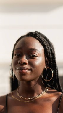 Saçları örgülü genç bir zenci kadının portresi. Evinin önünde bir yaz öğleden sonrasının tadını çıkarıyor.