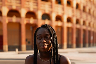 Saçları örgülü genç siyah bir kadın, öğleden sonranın tadını çıkarıyor, şehirdeki bir kahve dükkanının terasında oturuyor.