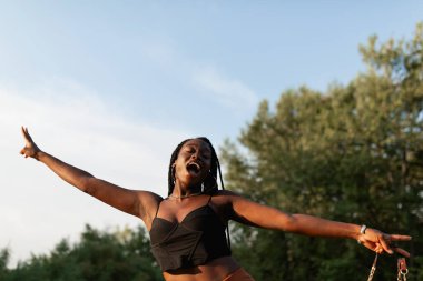 Saçları örgülü genç bir zenci kadın gün batımında parkta yürürken aylaklık ediyor.