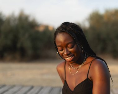 Saçları örgülü genç bir zenci kadın gün batımında yürüyüş yaparken dinleniyor ve dinleniyor.