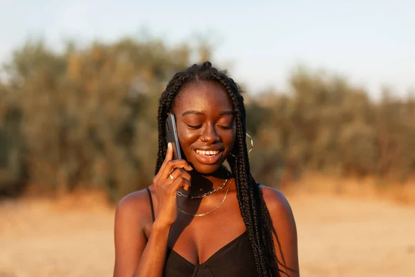 Young Black Woman Braids Her Hair Happily Talks Her Smartphone — Stock Photo, Image