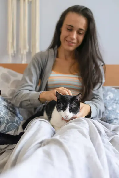A young woman, with a sleepy face, caresses her cat in bed, waking up in the morning.