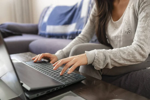 A woman surfs the Internet and types on the keyboard of her laptop while sitting on the sofa at home.