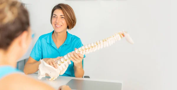 A physiotherapist explains to her patient the problem of low back pain and impingement in the vertebrae using an anatomical skeleton