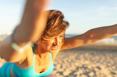 Bir kadın formda kalmak için plajda egzersiz ve pilates hareketleri yapıyor.
